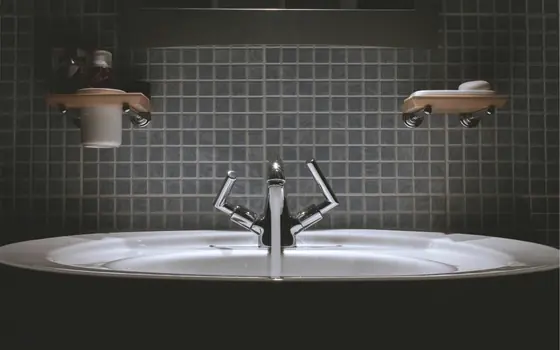 A basin and mixer faucet in a dark tiled bathroom