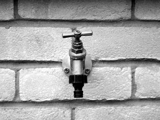 An outdoor hose bibb mounted on a painted brick wall
