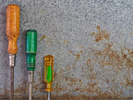 Screwdrivers and a hammer laid on a weathered steel sheet