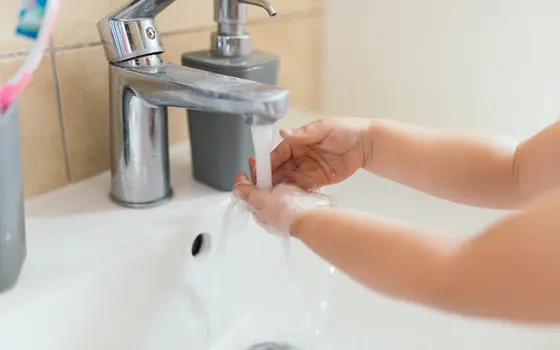 A child washing their hands under a running faucet